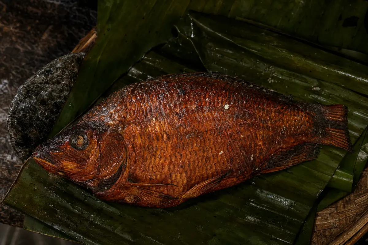 Un poisson entier fumé posé sur une feuille de bananier, la peau cuivrée et brillante.